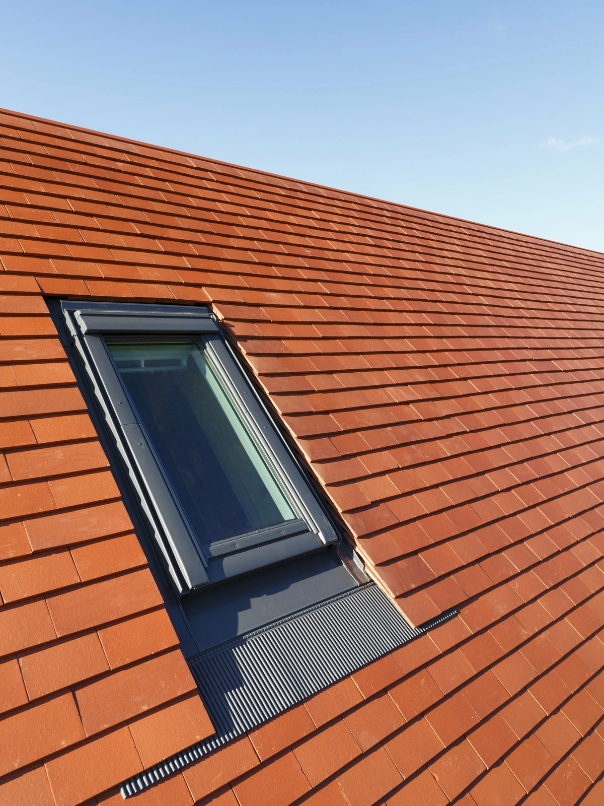 Fenêtre de toit installée sur une toiture en tuiles rouges sous un ciel bleu