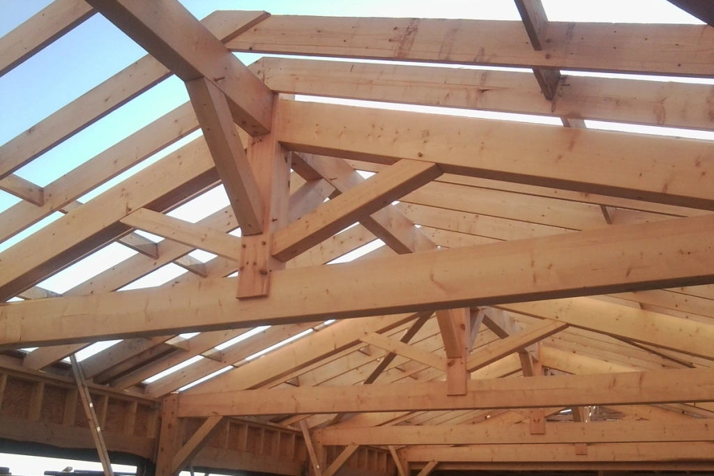 Vue intérieure d'une charpente en bois traditionnelle en cours de construction, montrant les poutres, les chevrons et les fermes qui forment la structure du toit.