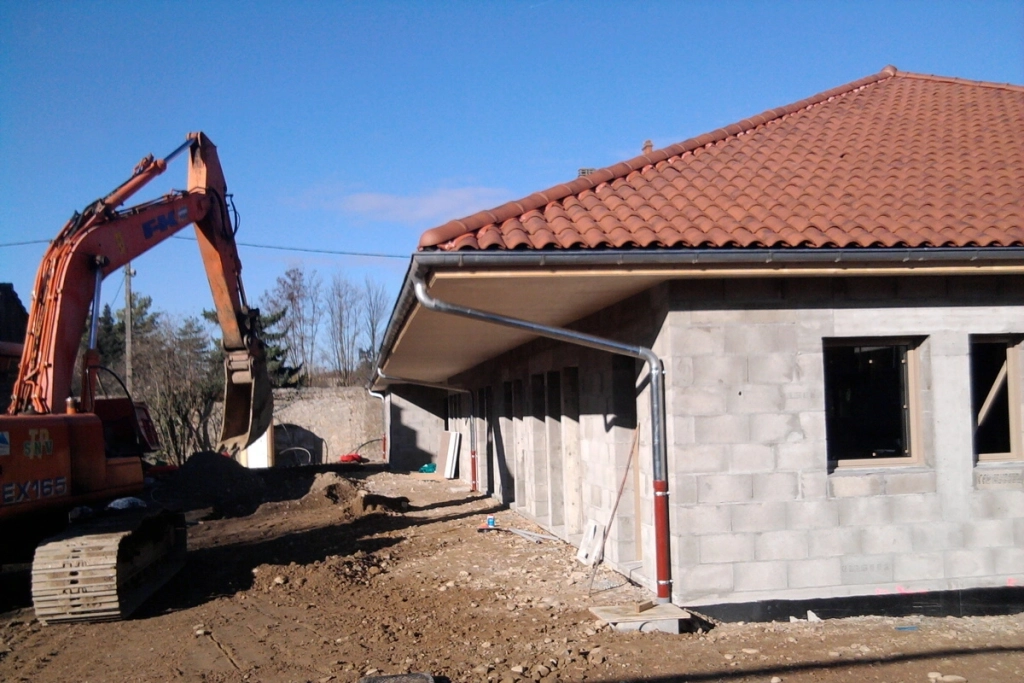 Construction d'une maison avec installation de gouttières et tuiles sur le toit, pelleteuse sur le chantier